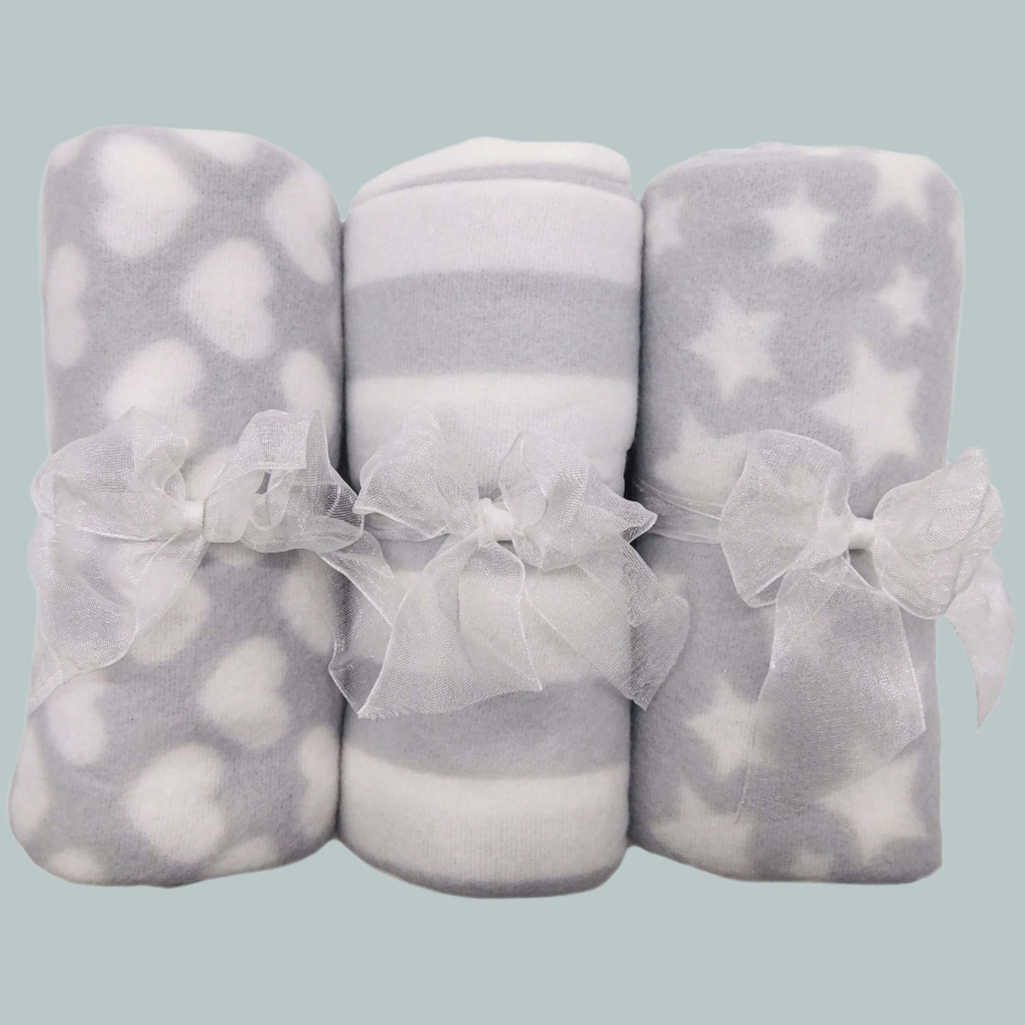 Three grey and white patterned blankets with sheer ribbons on a neutral background