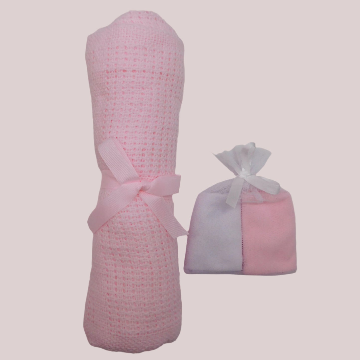 Pink knitted blanket with a bow and a pink and white washcloths on a pale pink background