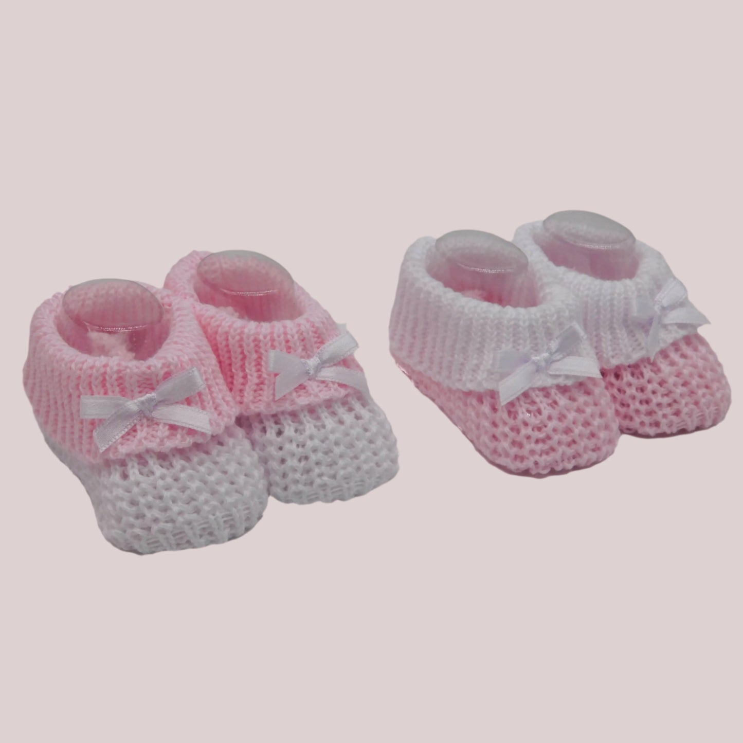 Pair of pink and white knitted baby booties with bows on a pale pink background