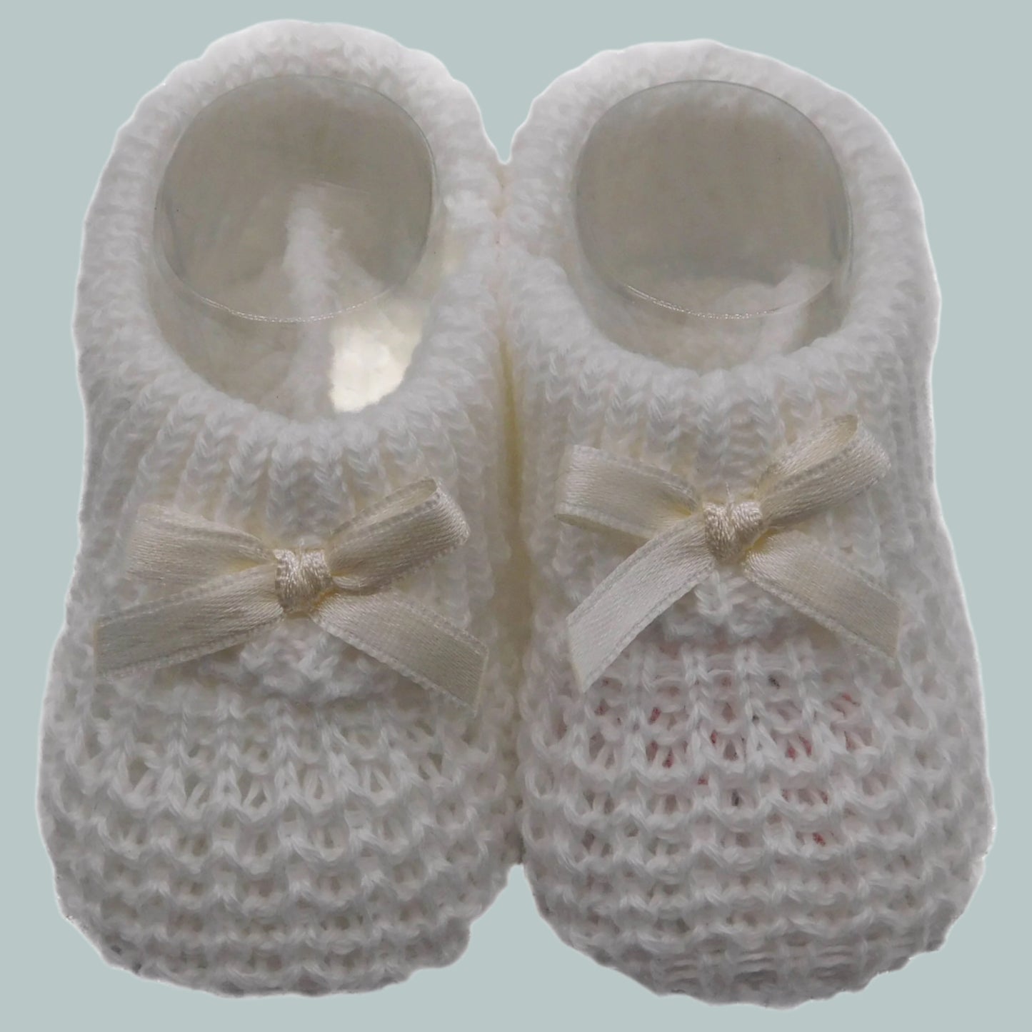 Pair of cream knitted baby booties with bow details on a neutral background