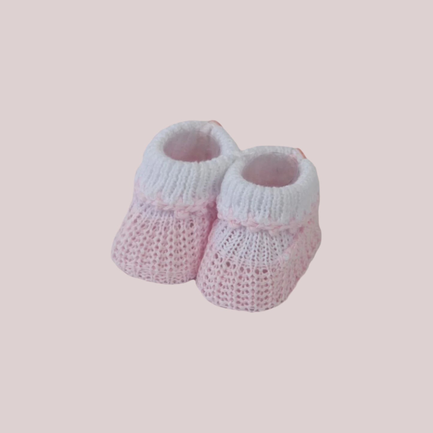 Pair of pink and white knitted baby booties on a light pink background