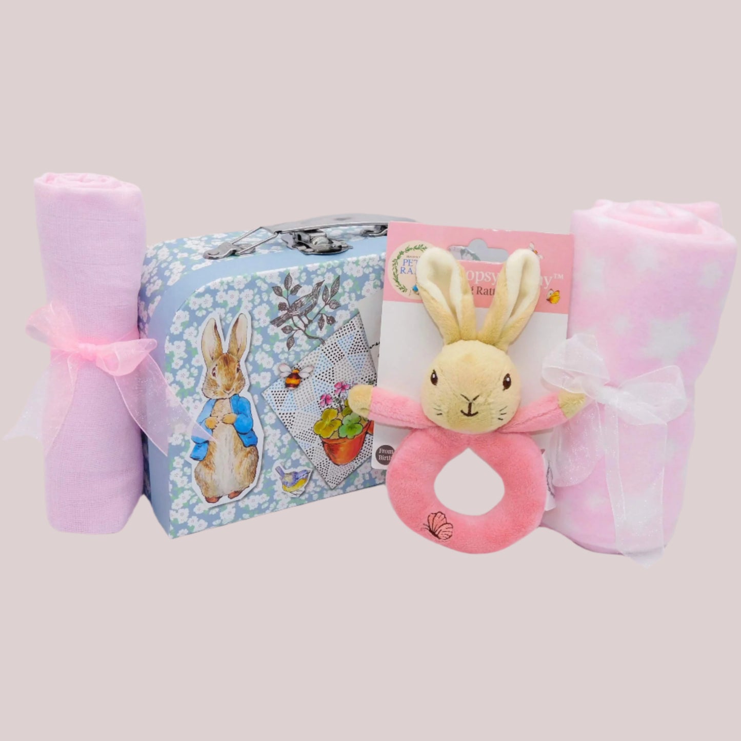 Baby gift set with plush Flopsy Bunny rattle, pink muslin square, and Peter Rabbit keepsake box on a pale pink background