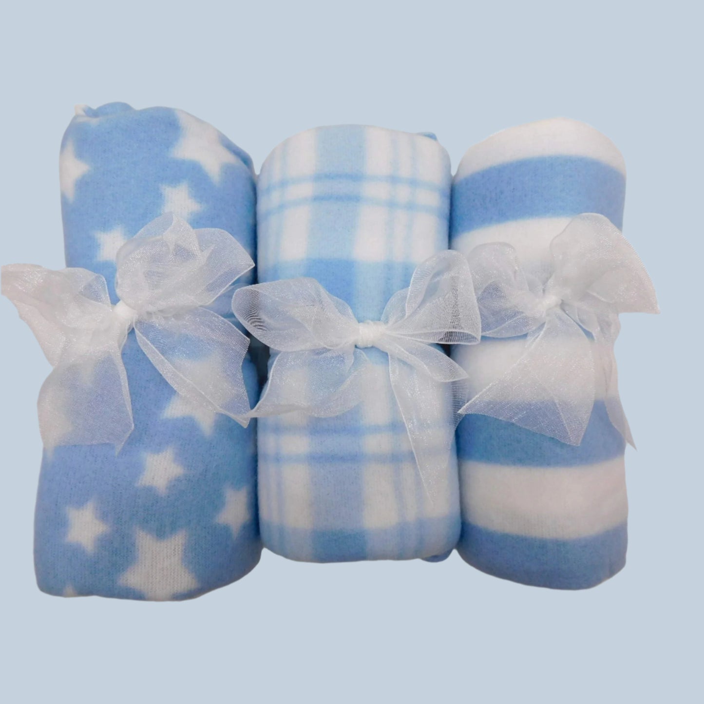 Baby blankets with different patterns in blue and white tied with ribbons on a pale blue background