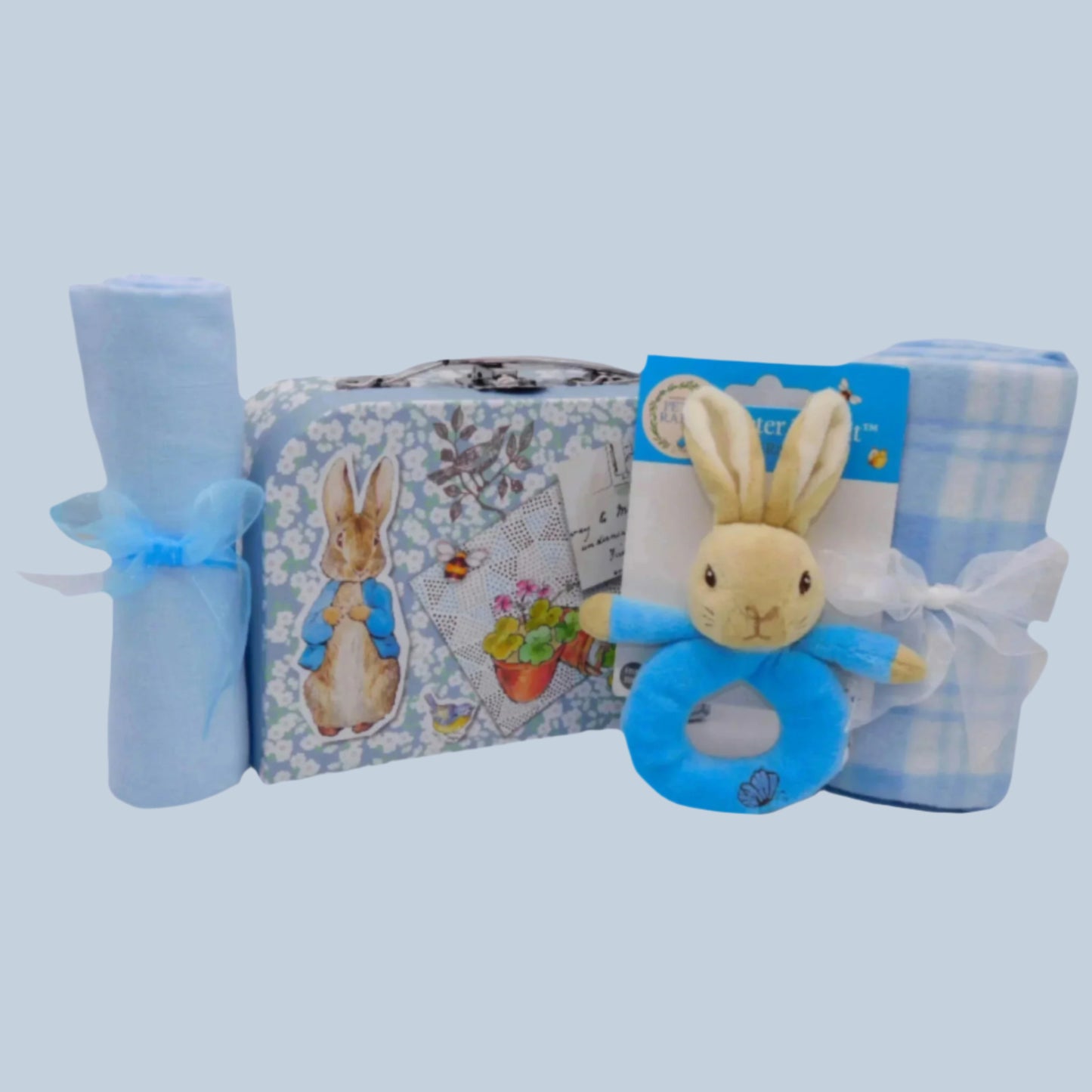 Peter Rabbit Baby gift set with blue plush Peter Rabbit ring rattle toy, blanket, and muslin on a pale blue background