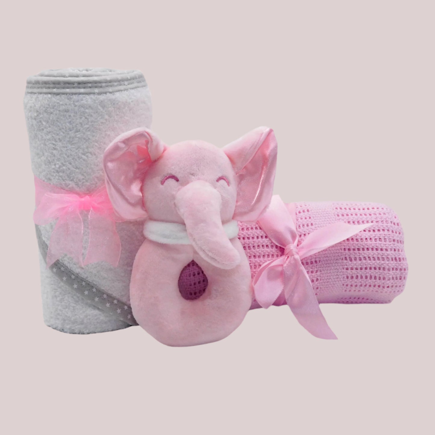 Pink elephant plush rattle toy with white towel and pink blanket on a pale pink background