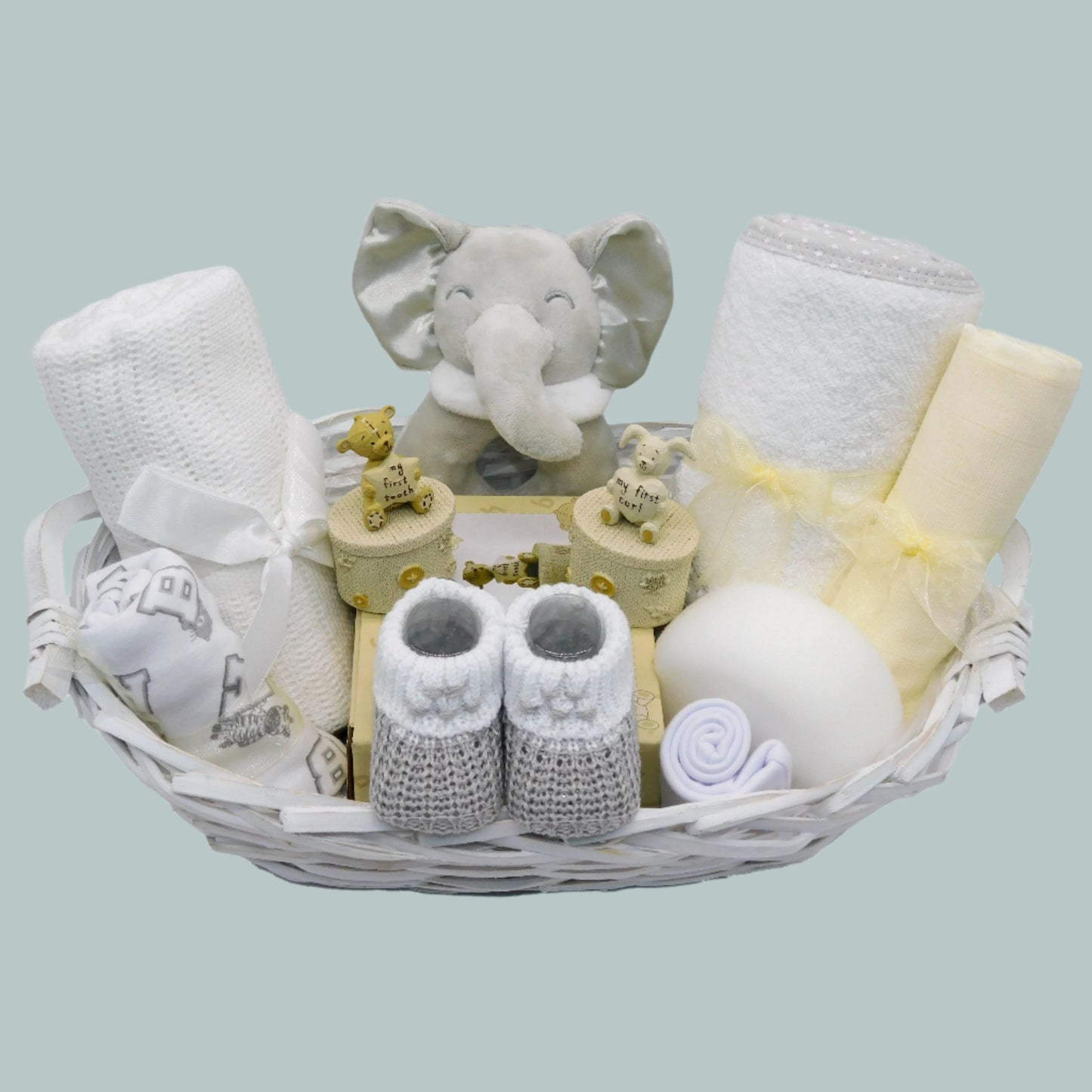 Unisex Baby gift basket with elephant toy rattle, booties, baby clothing and other baby essentials on a neutral background