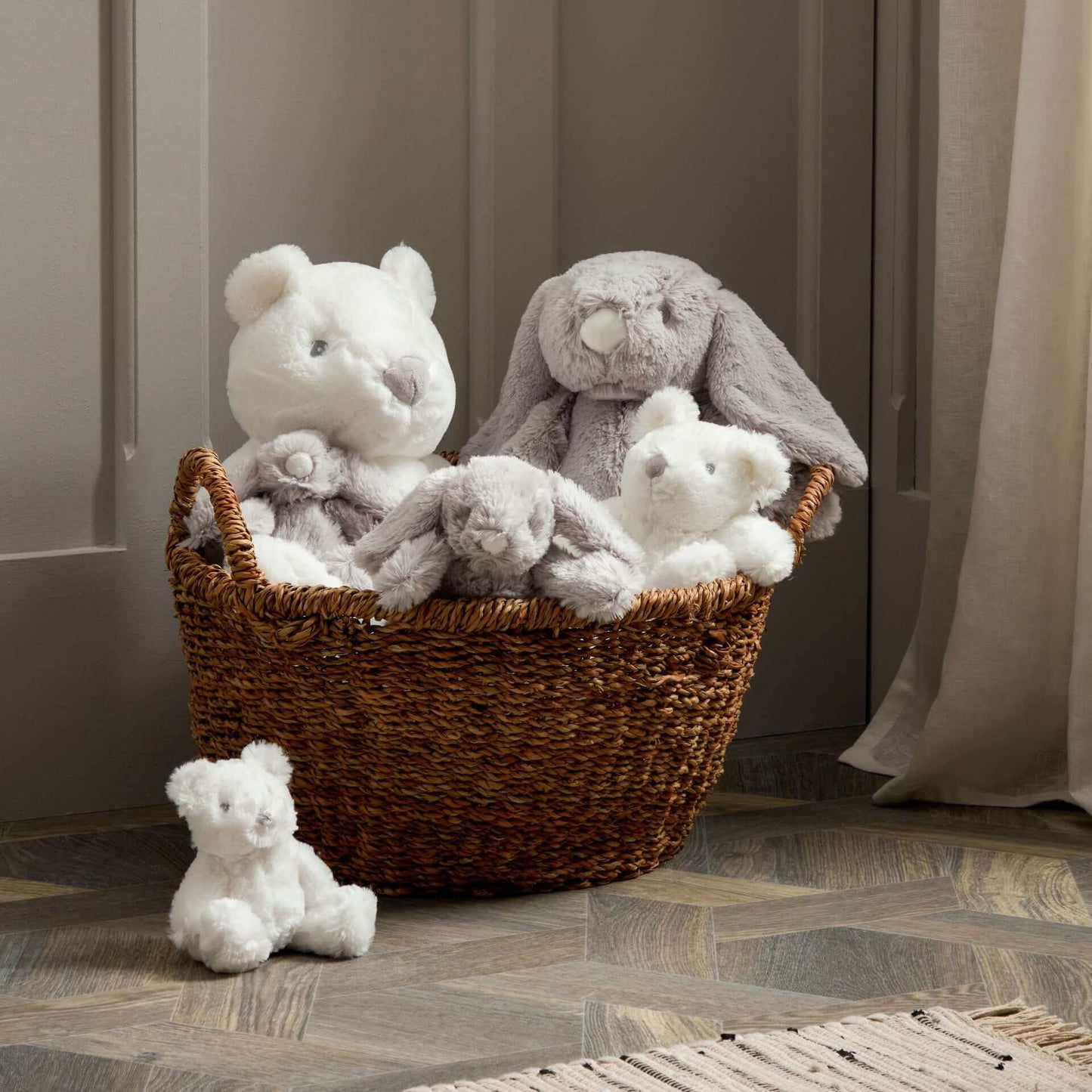 Selection of soft teddies and bunnies for newborns in a wicker basket