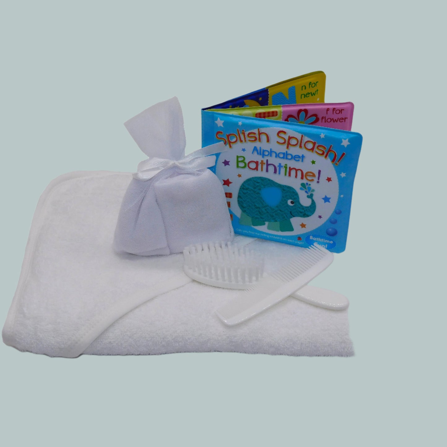Baby bath time set with white towel, washcloths, brush and comb, and bath book on a neutral background