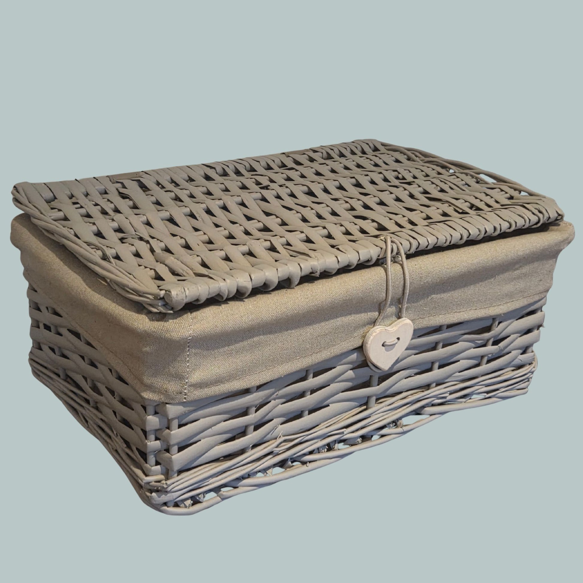 Grey wicker hamper basket with a closed lid, cotton lining and heart clasp 