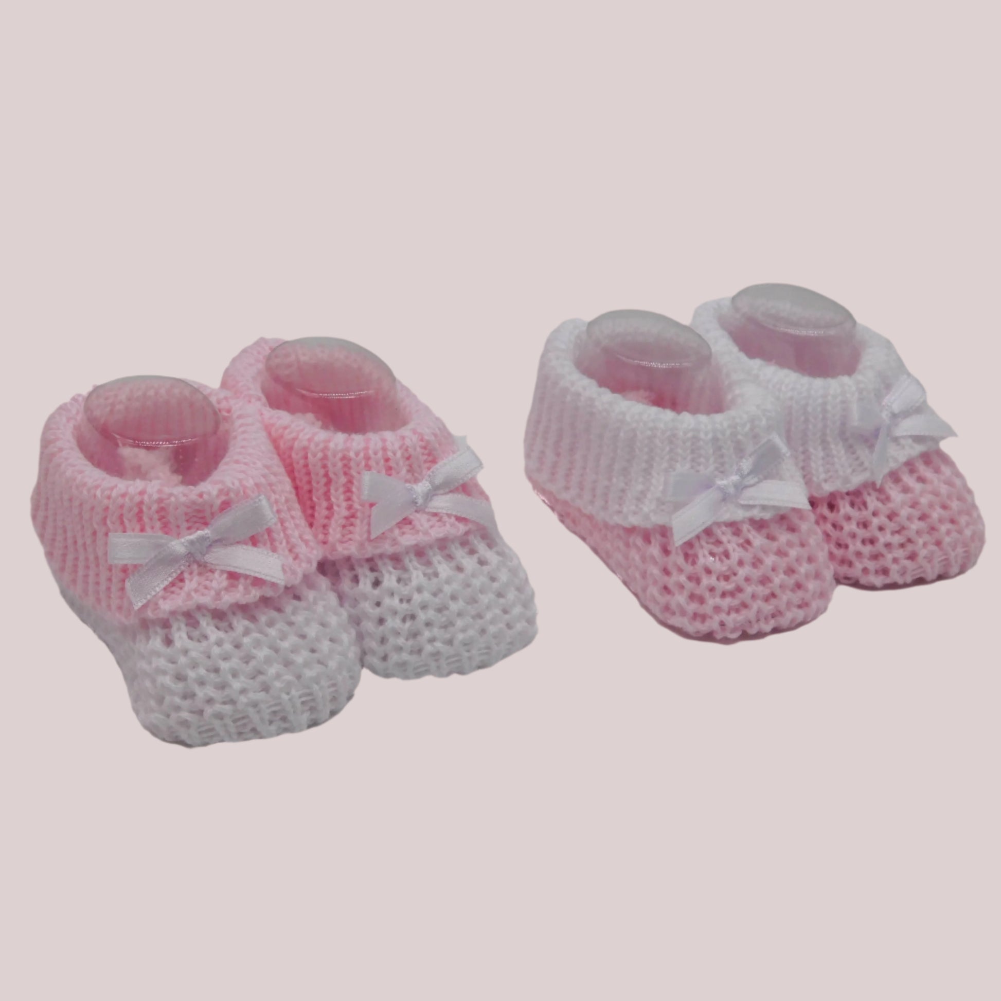 Pair of pink and white knitted baby booties with bows on a pale pink background