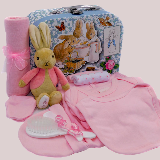 Baby gift set in a keepsake suitcase with plush Flopsy Bunny toy bean rattle, muslin square, brush and comb, and clothing set on a pale pink background