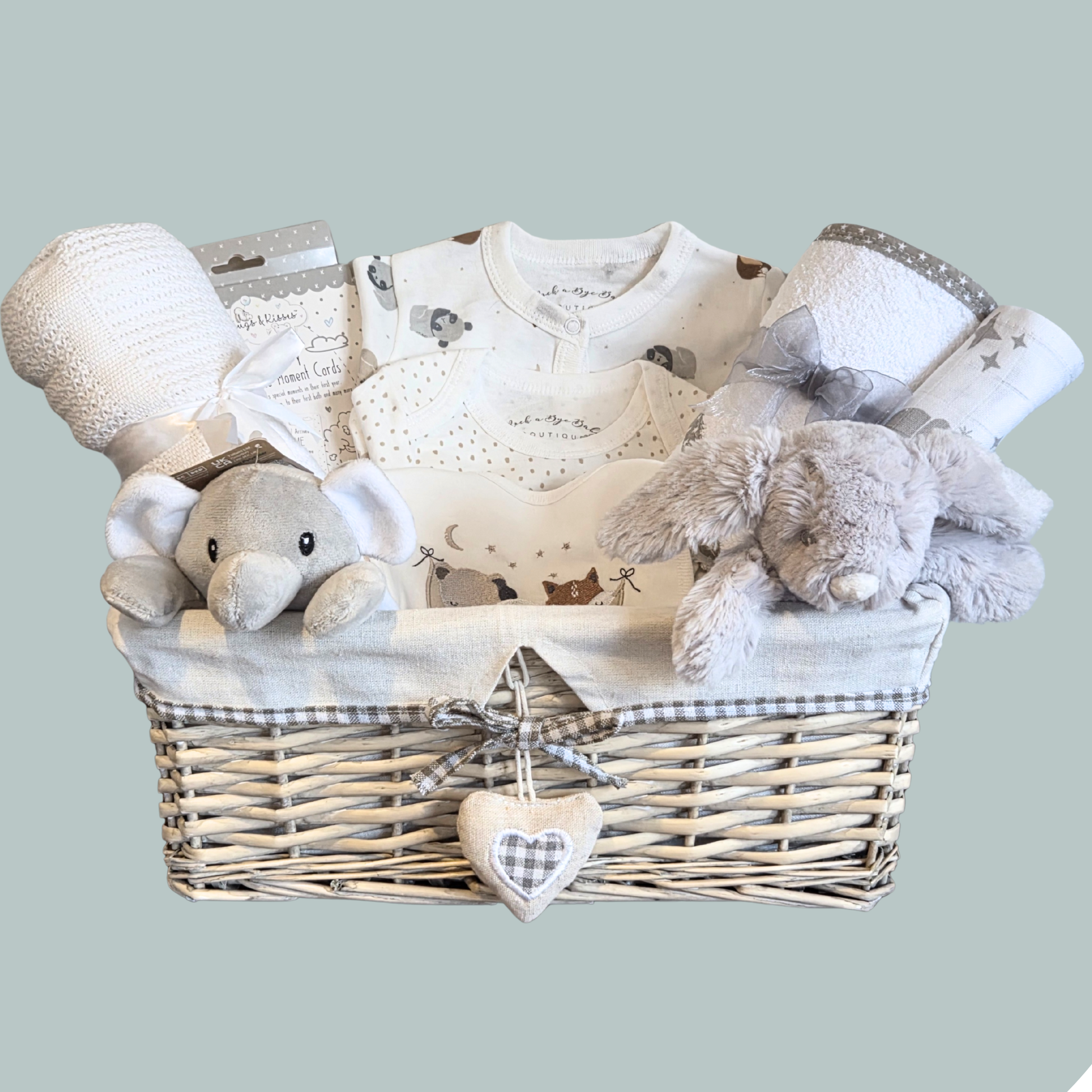 Baby gift basket with plush toys, clothes, blanket and towel on a light teal background
