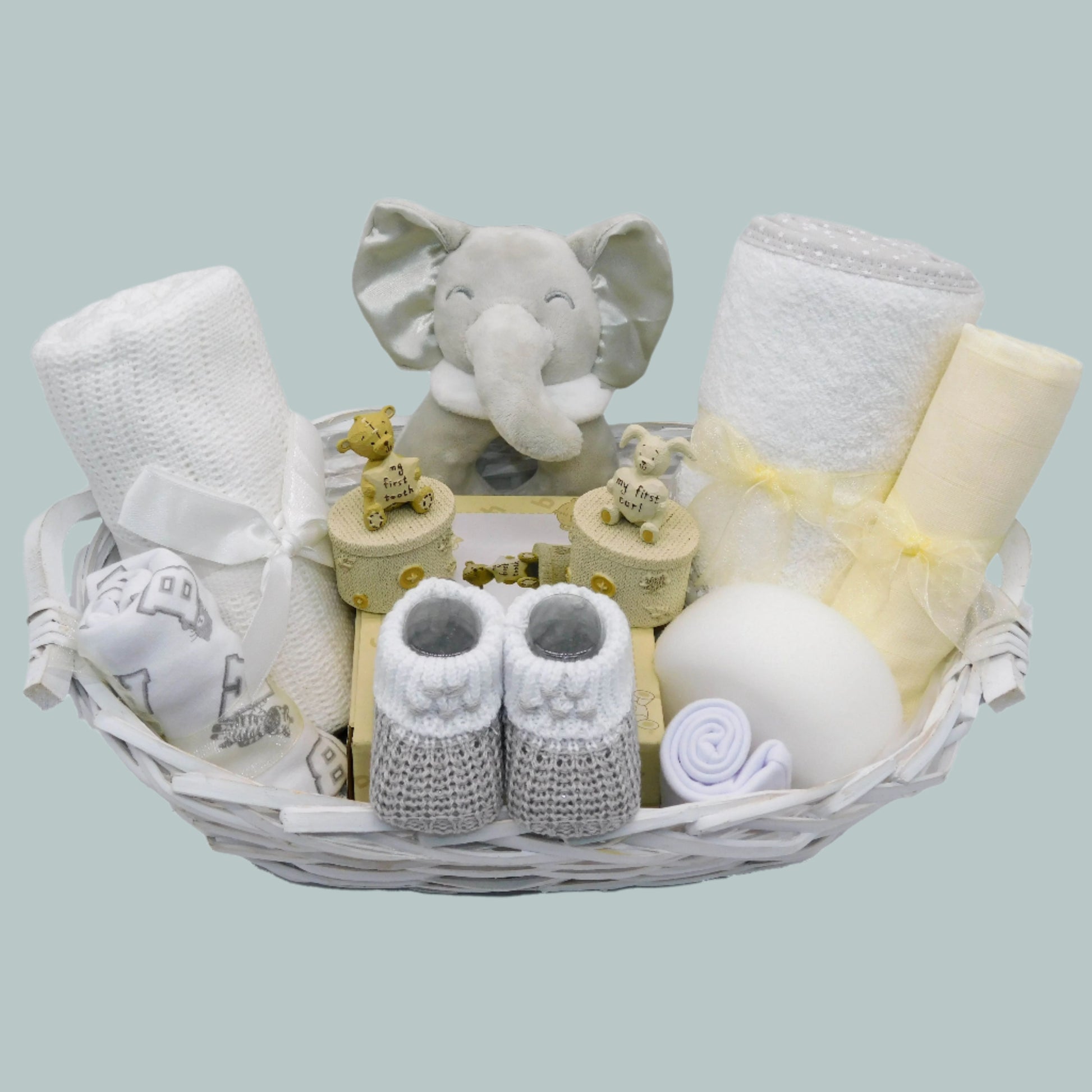 Unisex Baby gift basket with elephant toy rattle, booties, baby clothing and other baby essentials on a neutral background
