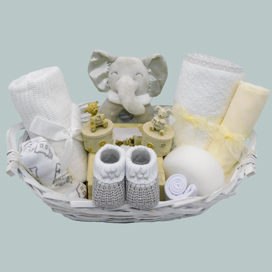 Unisex Baby gift basket with elephant toy rattle, booties, baby clothing and other baby essentials on a neutral background