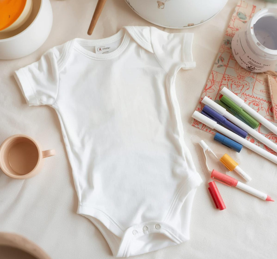 A white babygro and coloured pens to decorate at a baby shower party